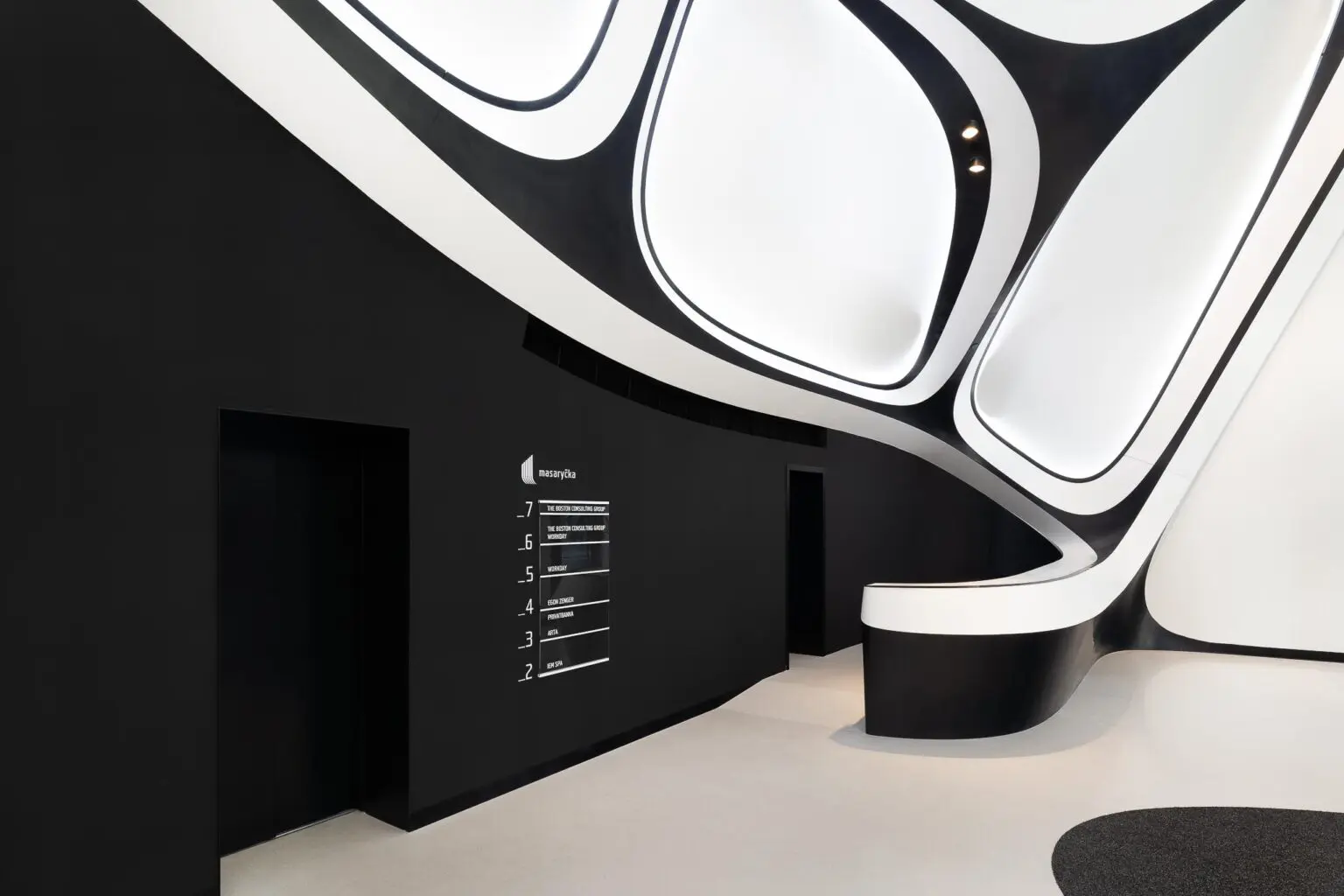 Futuristický interiér Masaryčky s černými a bílými zakřivenými liniemi a minimalistickým designem.