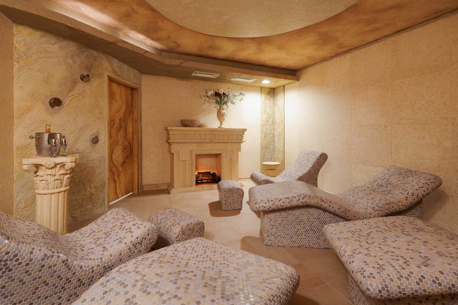 Luxusní moderní interiér wellness s elegantními lehátky a dekorativním krbem.