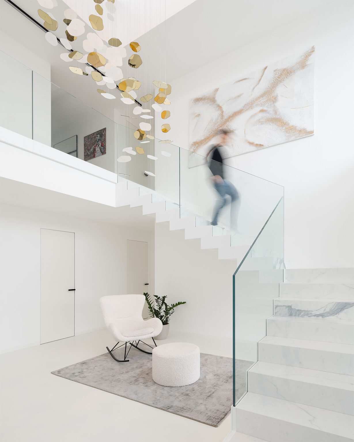 Moderní minimalistický interiér se schodištěm a skleněným zábradlím. Designové osvětlení.